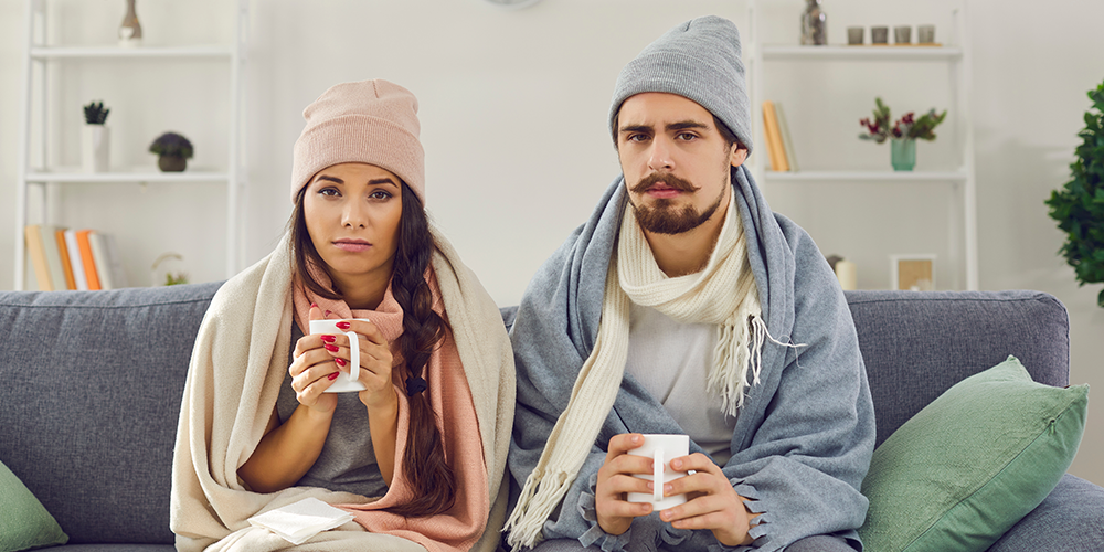 Young couple bundled up on couch because furnace is blowing cold air.