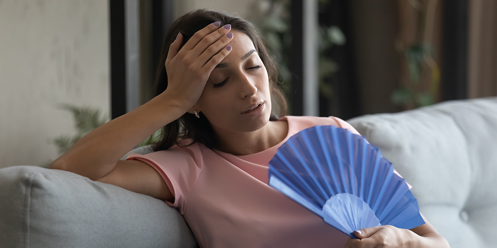 Woman in pink fans herself on couch while wondering how to lower home humidity.