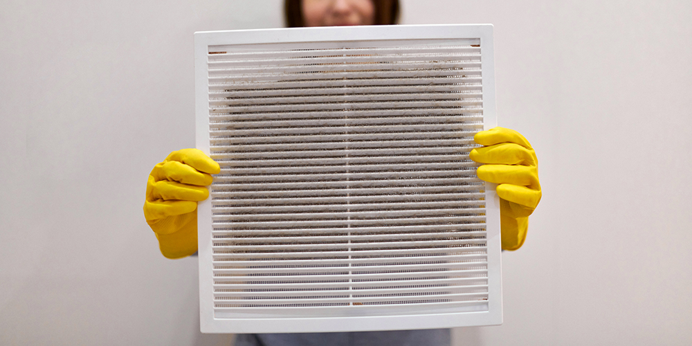 Homeowner in yellow gloves performs air filter replacement.